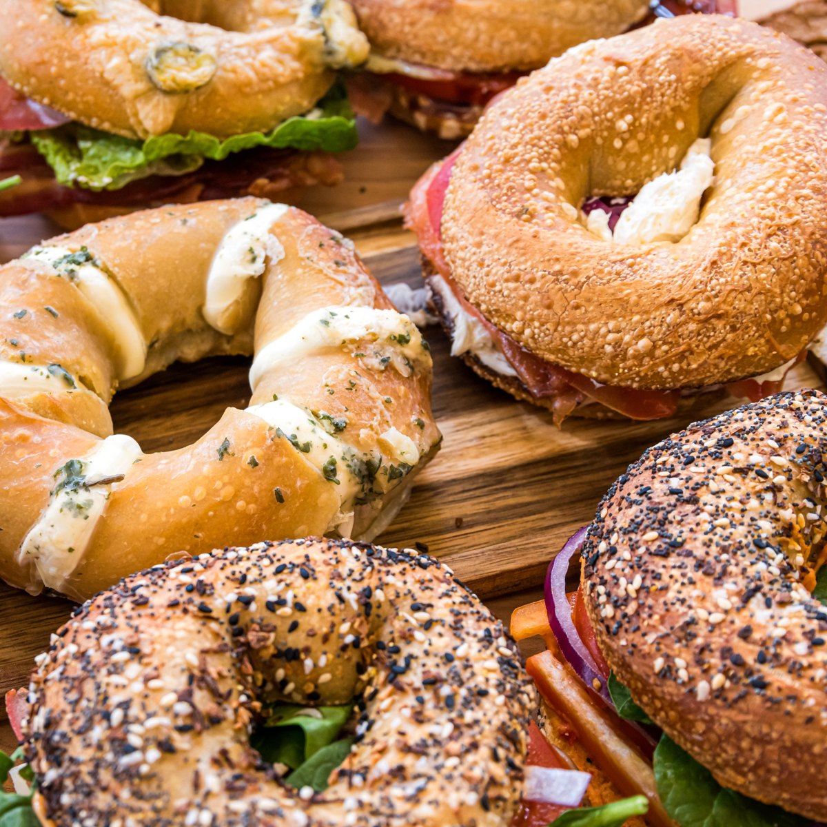 An assortment of freshly prepared bagel sandwiches with cream cheese, vegetables and deli fillings.
